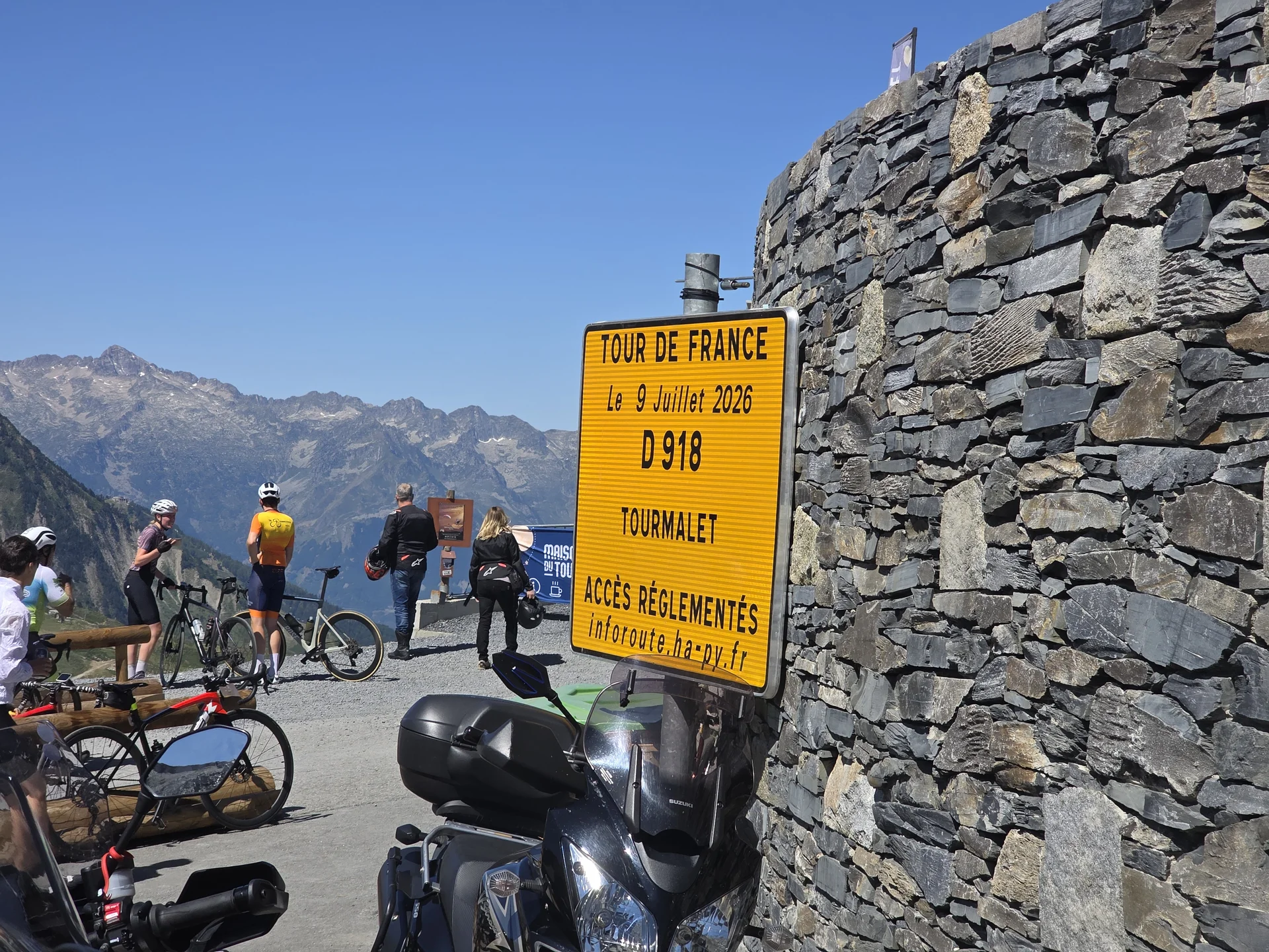 Hinweisschild zur Tour de France am Col du Tourmalet zwischen Radfahrern und Motorrädern