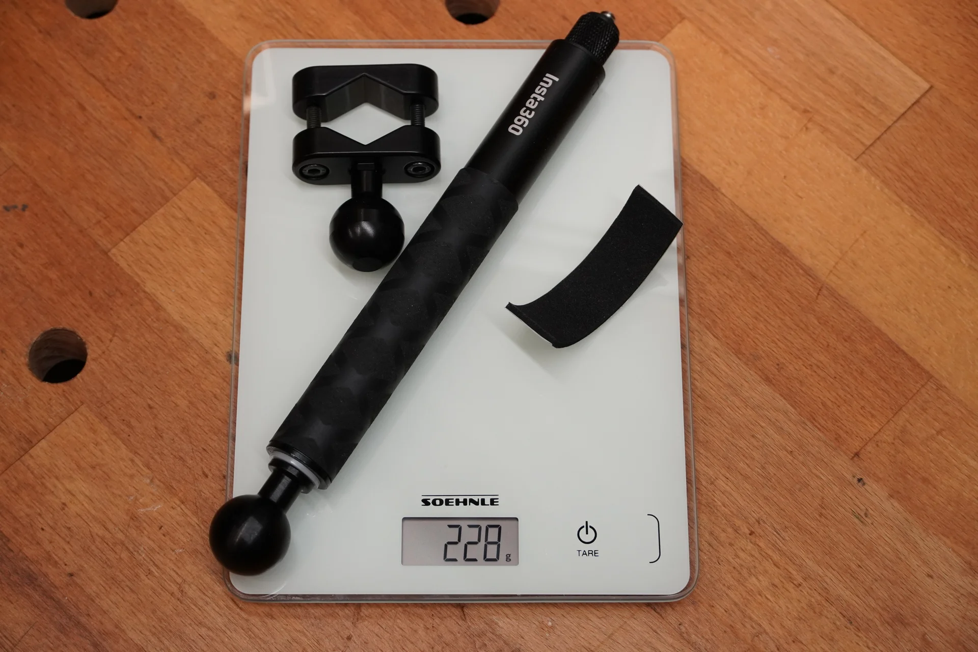 Insta360-Teleskopstab mit Kugelkopf und Kugelflex-Klemmschelle auf einer Digitalwaage, die 228 Gramm anzeigt.