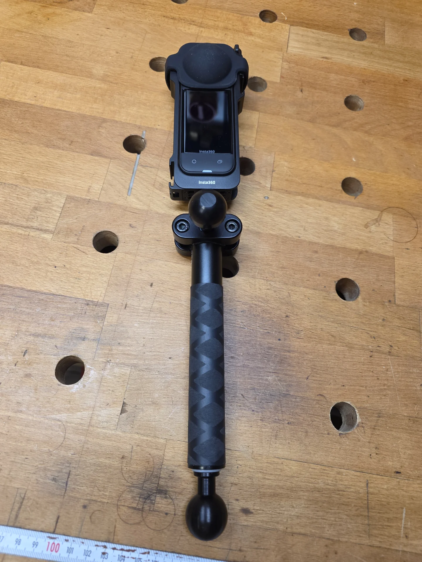 Insta360 X5 mit sichtbarem Display und Kugelflex-Halterung auf einem Teleskopstab, fotografiert von vorne.