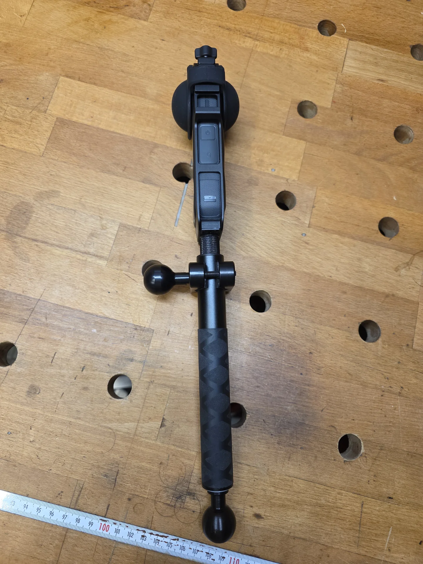 Insta360 X5 von der schmalen Seite mit Kugelflex-Klemmschelle und Teleskopstab auf einer Werkbank.